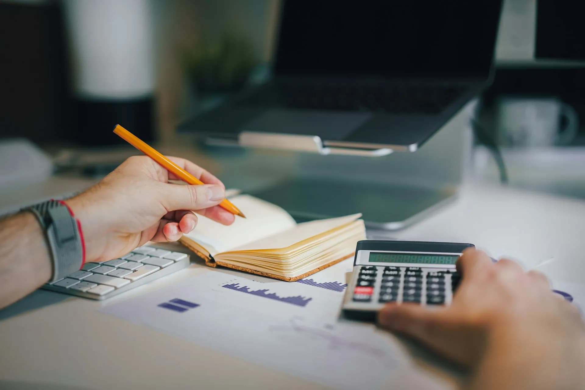 Hands working through figures with a pencil, notebook and calculator