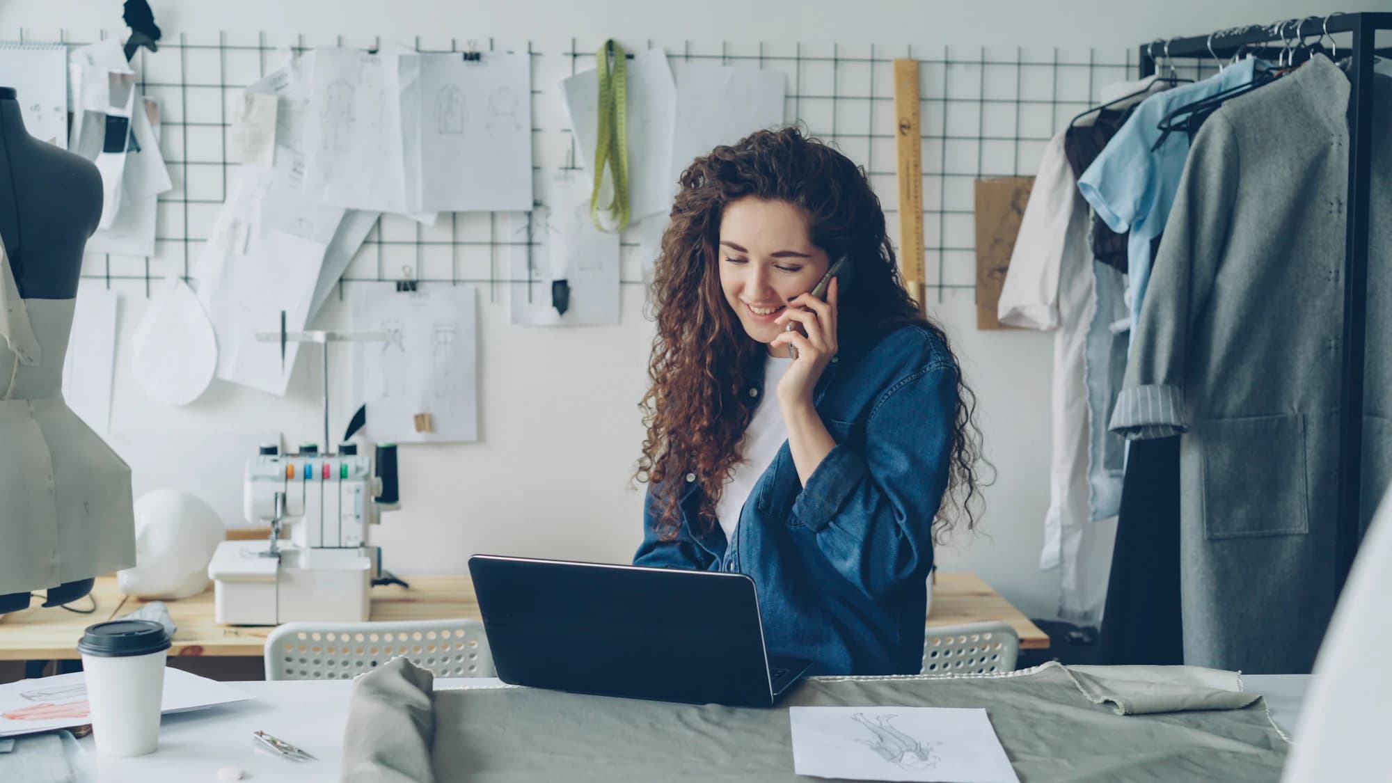 A shop owner on the phone at her laptop in a clothing studio